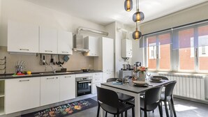 Een moderne keuken met witte kasten, een eettafel met stoelen en hanglampen.