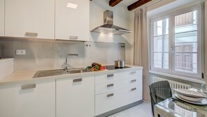 Une cuisine moderne avec des meubles blancs, une hotte de cuisinière en acier inoxydable et une fenêtre avec des rideaux.