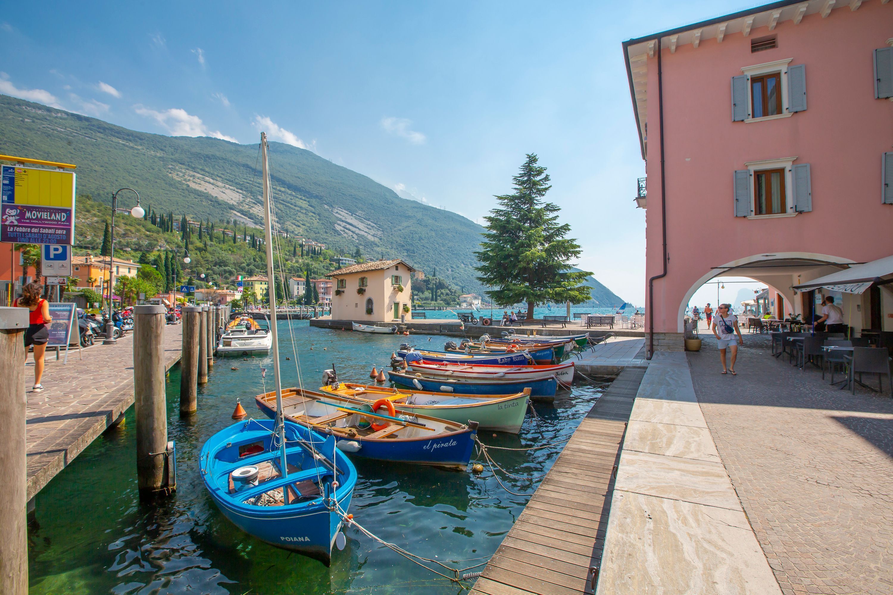 A waterfront scene with boats docked at a pier, a mountain in the background, and a building with a pink facade.