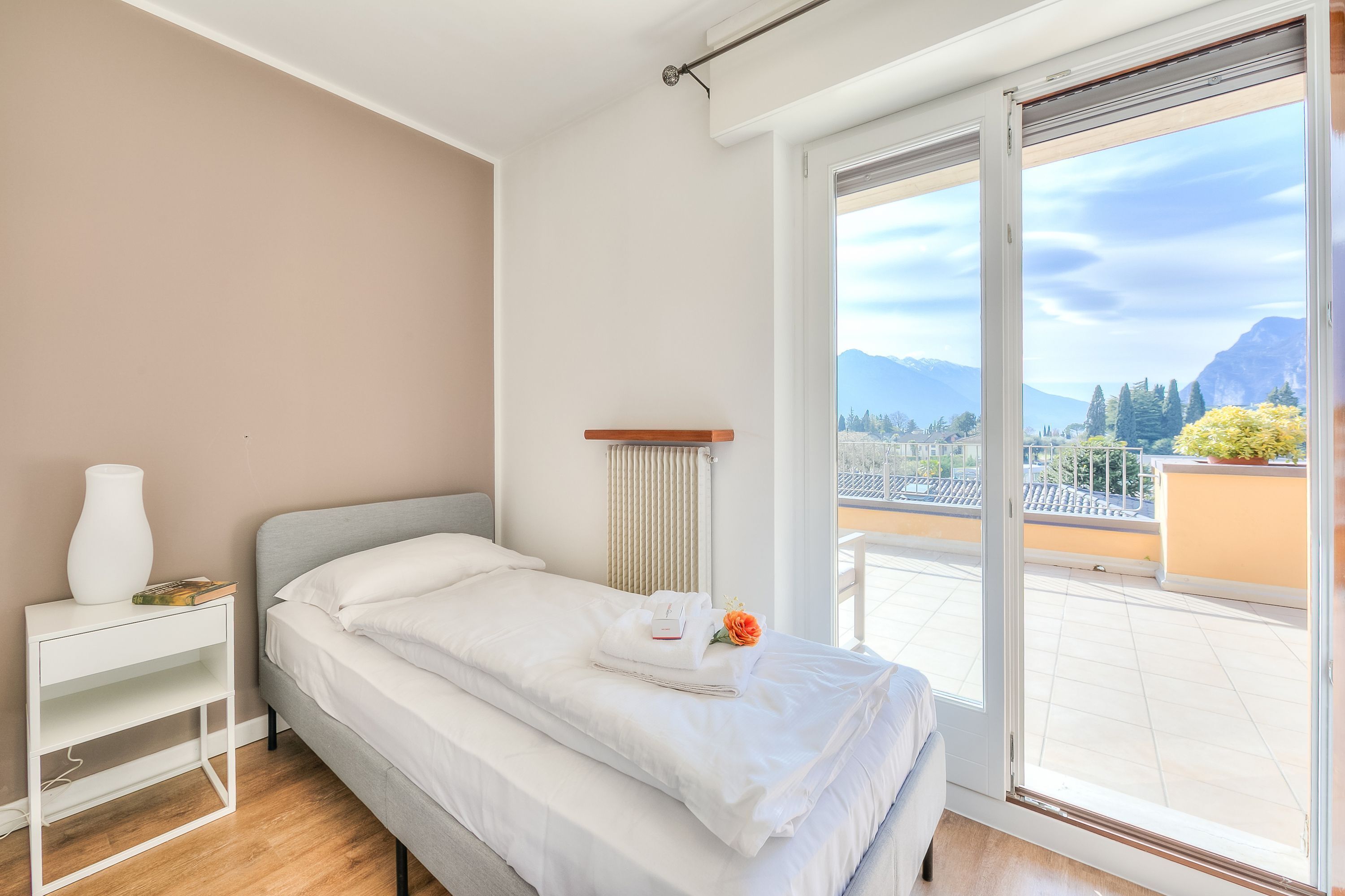 Una camera da letto con un letto, un comodino, un termosifone e vista su un balcone con montagne.