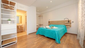 Un dormitorio con cama, armario blanco, baño y suelo de madera.