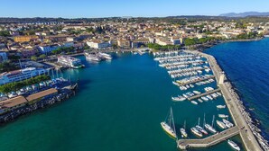 An aerial view of a marina with numerous boats docked, surrounded by a coastal town with buildings and a clear sky. - Borgo Degli Ulivi in Toscolano Maderno (Toscolano Maderno)