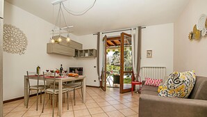 A dining area with a table set for four, a sofa, and a view of the outdoors through a glass door. - Borgo Degli Ulivi in Toscolano Maderno (Toscolano Maderno)
