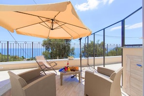 Een balkon met rieten meubels, een tafel met drankjes en een grote parasol.