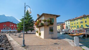 A cobblestone waterfront with colorful buildings, a street lamp, and a row of benches. - Riva Lago e Spiaggia Apartment (Riva del Garda)