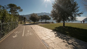 A paved path with bicycle lanes and a grassy area beside a body of water. - Riva Lago e Spiaggia Apartment (Riva del Garda)