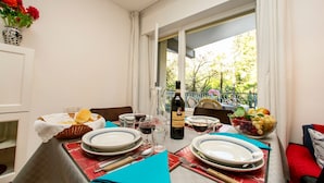 A dining table set with plates, glasses, and a bottle of wine, with a view of trees and a balcony outside. - Riva Lago e Spiaggia Apartment (Riva del Garda)