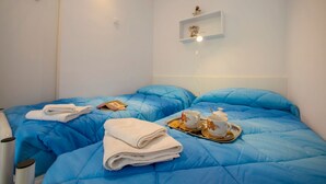 A hotel room with a blue bedspread, a tray with two cups and a teapot, and folded towels on the bed. - Riva Lago e Spiaggia Apartment (Riva del Garda)