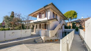Ein zweistöckiges Haus mit Balkon, Treppe und einer gepflasterten Fläche mit Blumentöpfen.
