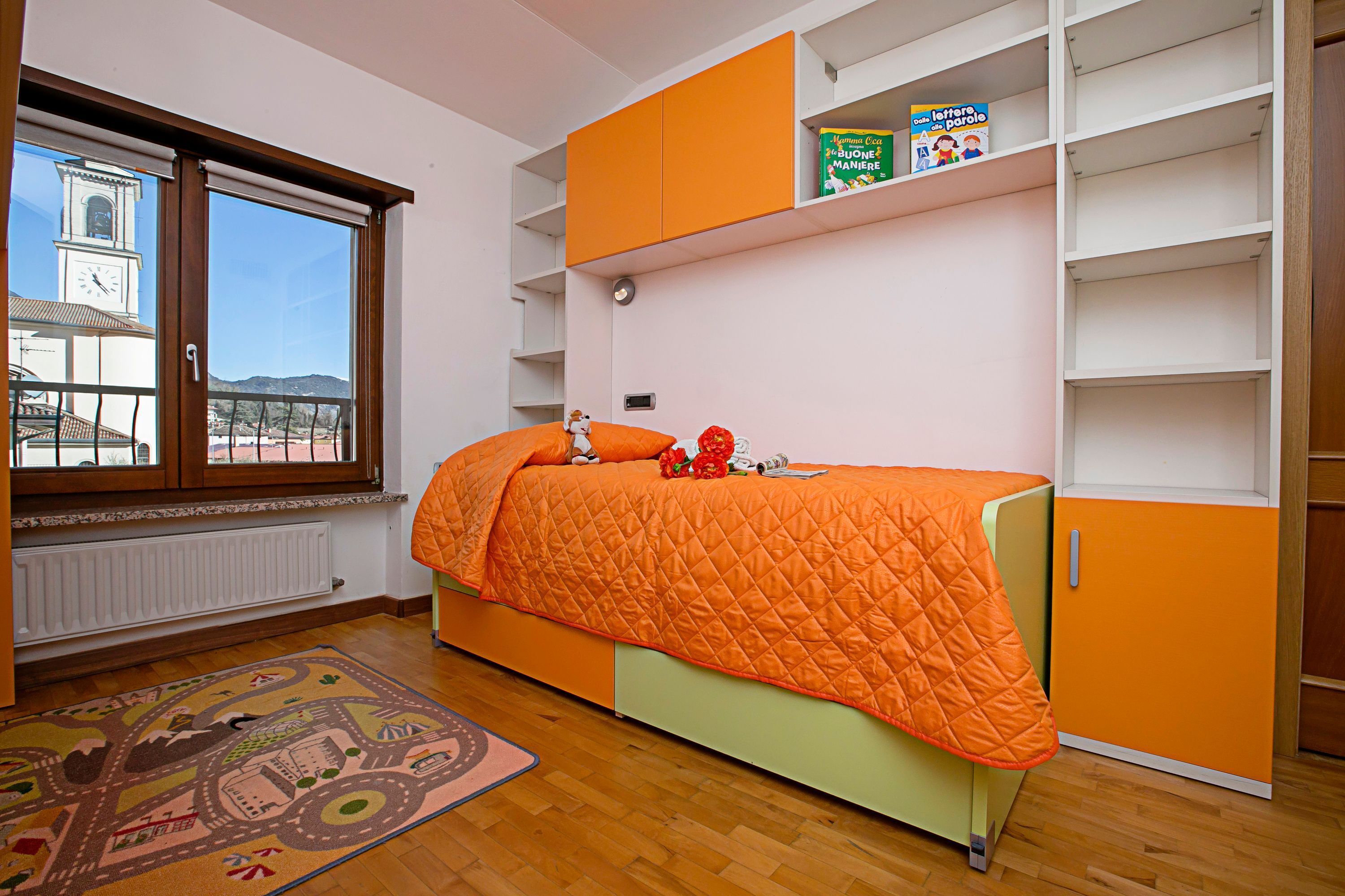 A bedroom with a bed, a window, a radiator, and a bookshelf.