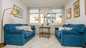 A room with two blue sofas, a wooden table, a floor lamp, and a window with curtains. - Riva Centro Apartment (Riva del Garda)