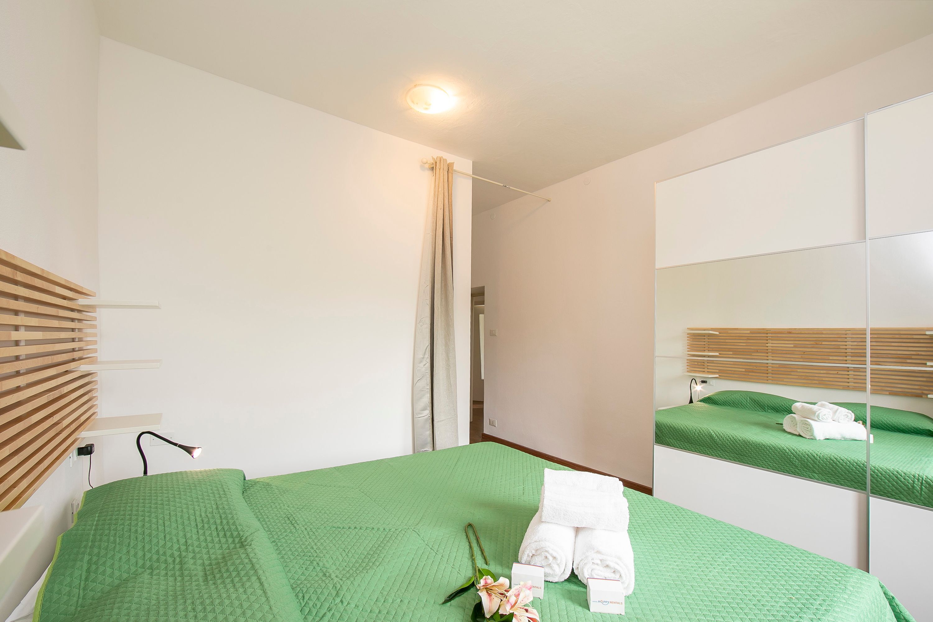 A hotel room with a green bedspread, a mirror, a wooden headboard, and a shower curtain.