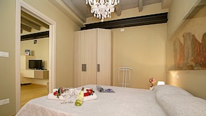 Une chambre à coucher avec un grand lit, un lustre, un tableau au mur et un téléviseur dans la pièce adjacente.