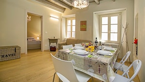 Un coin repas avec une table dressée pour quatre personnes, un lustre et une vue sur une chambre à coucher par une porte ouverte.