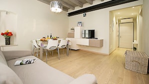 Un salon moderne comprenant un canapé, une table à manger, des chaises, un téléviseur et un panier en osier.