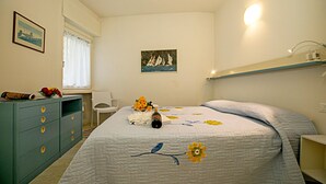 A bedroom with a bed, a dresser, a chair, a painting, and a shelf. - Riva Lago e Spiaggia Apartment 3 (Riva del Garda)