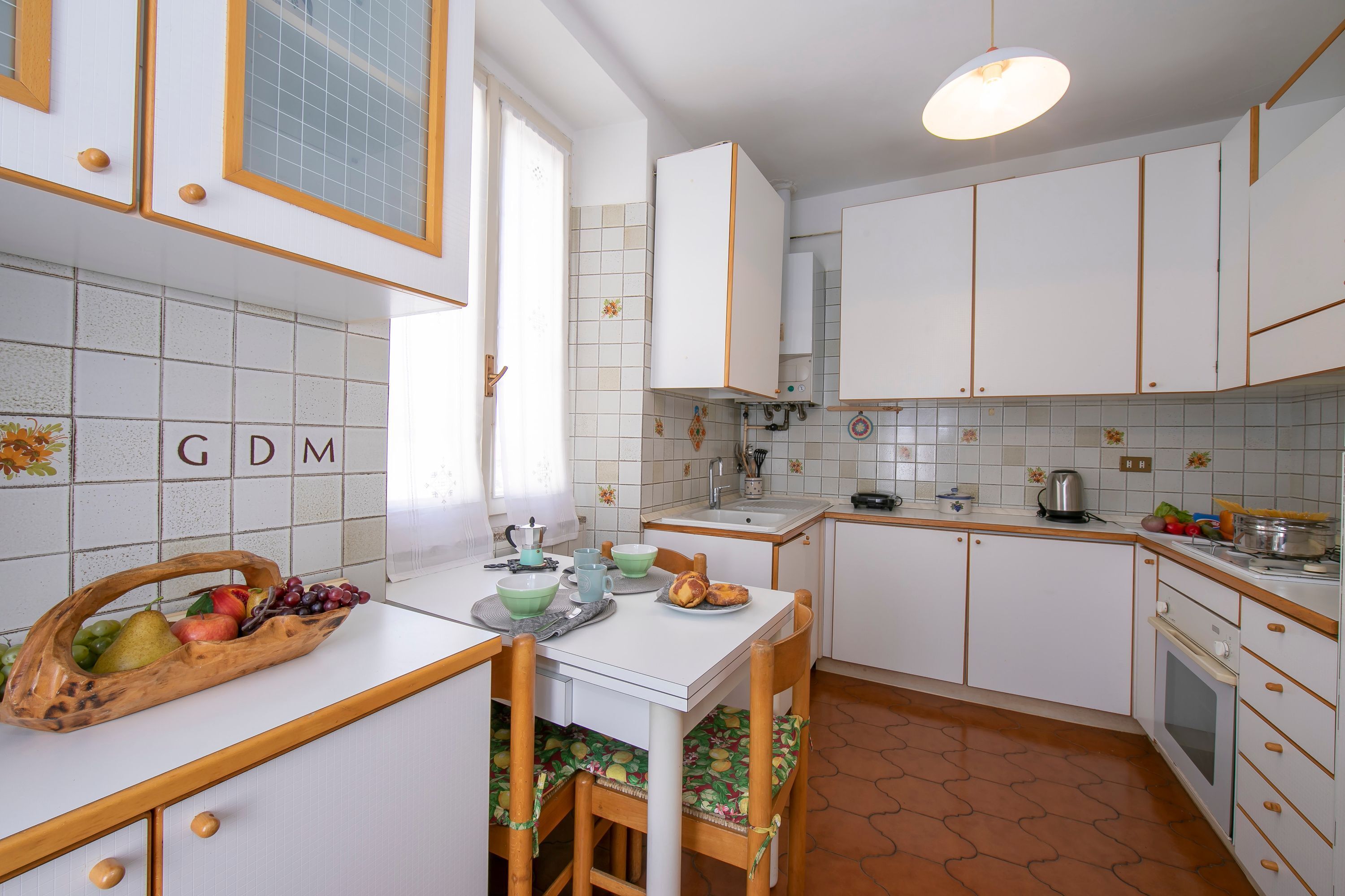 A kitchen with white cabinets, a tiled backsplash, and a fruit basket on the counter.