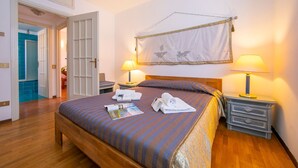 A neatly made bed with a striped bedspread, two bedside lamps, a wooden nightstand, and a wall-mounted tapestry. - Easy Central Stresa in Stresa (Stresa)