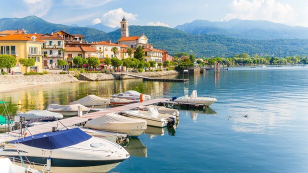 A marina with boats docked, a waterfront promenade, and buildings with a prominent tower in the background. - Easy Central Stresa in Stresa (Stresa)