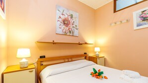 Een hotelkamer met een bed, nachtlampjes, een nachtkastje, een wandplank en een bloemschilderij.