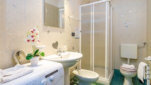 Een moderne badkamer met douche, toilet, wastafel en een wasmachine.