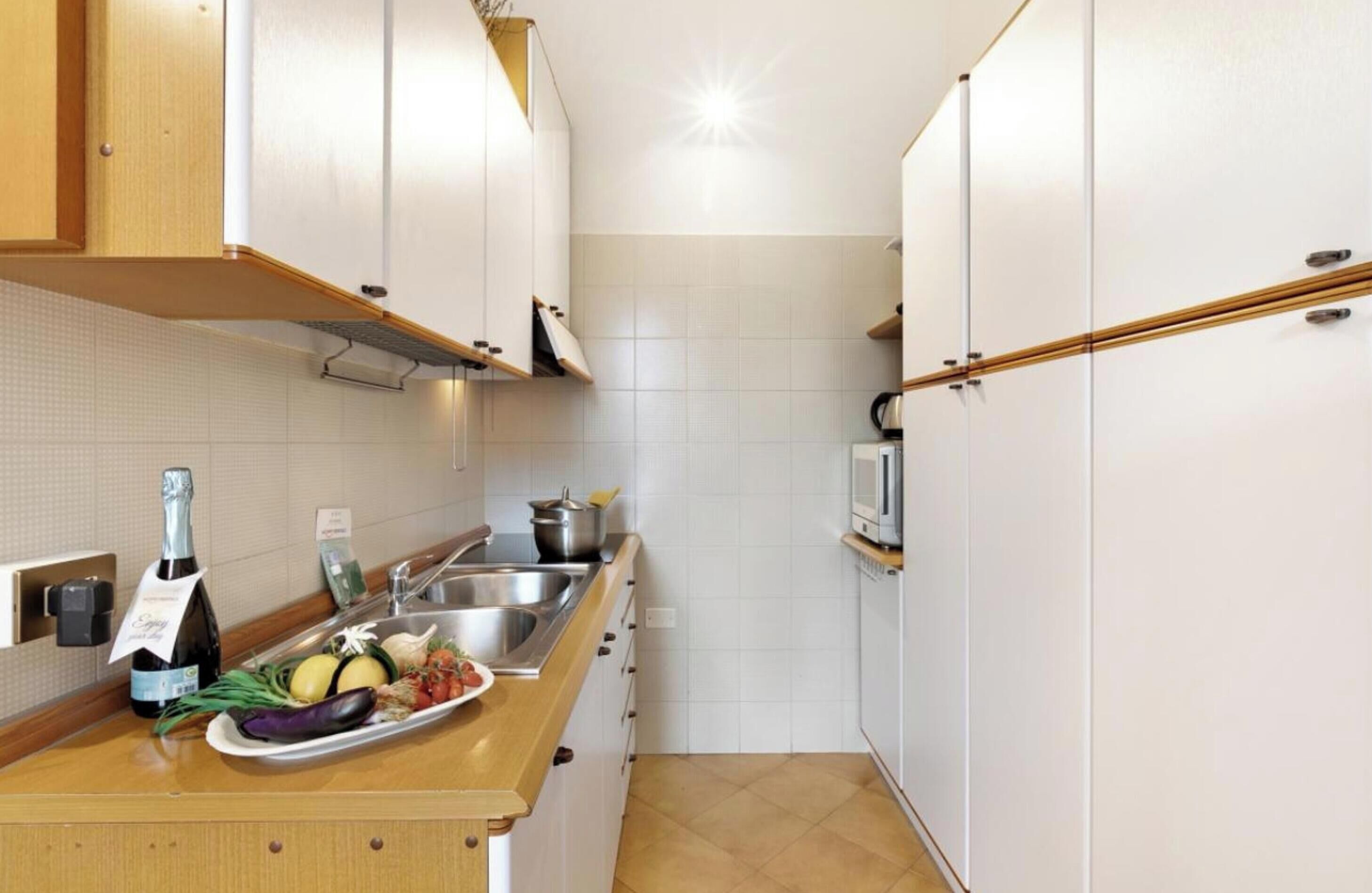 Eine schmale Küche mit weißen Schränken, einer Holz Arbeitsplatte, einer Spüle und einer Mikrowelle.