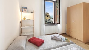 A bedroom with a bed, a wardrobe, a radiator, and a window with a view of buildings. - Lake View Historical Center Apartment (Riva del Garda)