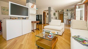 Ett modernt vardagsrum med en stor tv-skärm, ett soffbord i glas, en vit soffa och en bokhylla full med böcker.