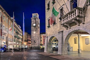 Una plaza histórica con una torre del reloj, edificios de piedra y zonas de estar al aire libre.