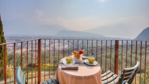 A table with a view of a valley and mountains, a bowl of fruit, and two cups on a balcony. - Lake View Dom-us Apartment (Riva del Garda)