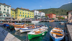 A marina with various boats docked, surrounded by colorful buildings and a hilly backdrop. - Lake View Dom-us Apartment (Riva del Garda)
