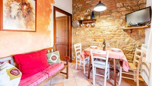 Ein gemütlicher Essbereich mit Steinwand, Holztisch mit rosa Tischdecke, weißen Stühlen und einem an der Wand befestigten Fernseher.