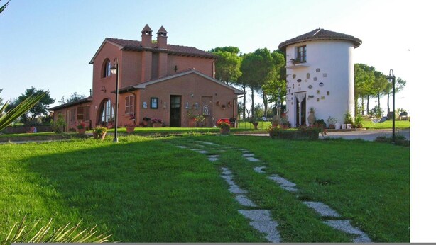 A brick building with a white cylindrical structure, surrounded by a well-maintained lawn and garden. - Myrtle apt With Shared Pool (Castiglione del Lago)