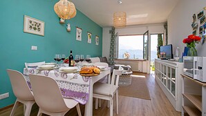 Un'area pranzo con un tavolo apparecchiato per due persone, una lampada appesa in vimini e una vista attraverso una porta aperta su un balcone.