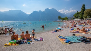 Ein überfüllter Strand mit badenden und sonnenden Menschen, umgeben von Bergen.