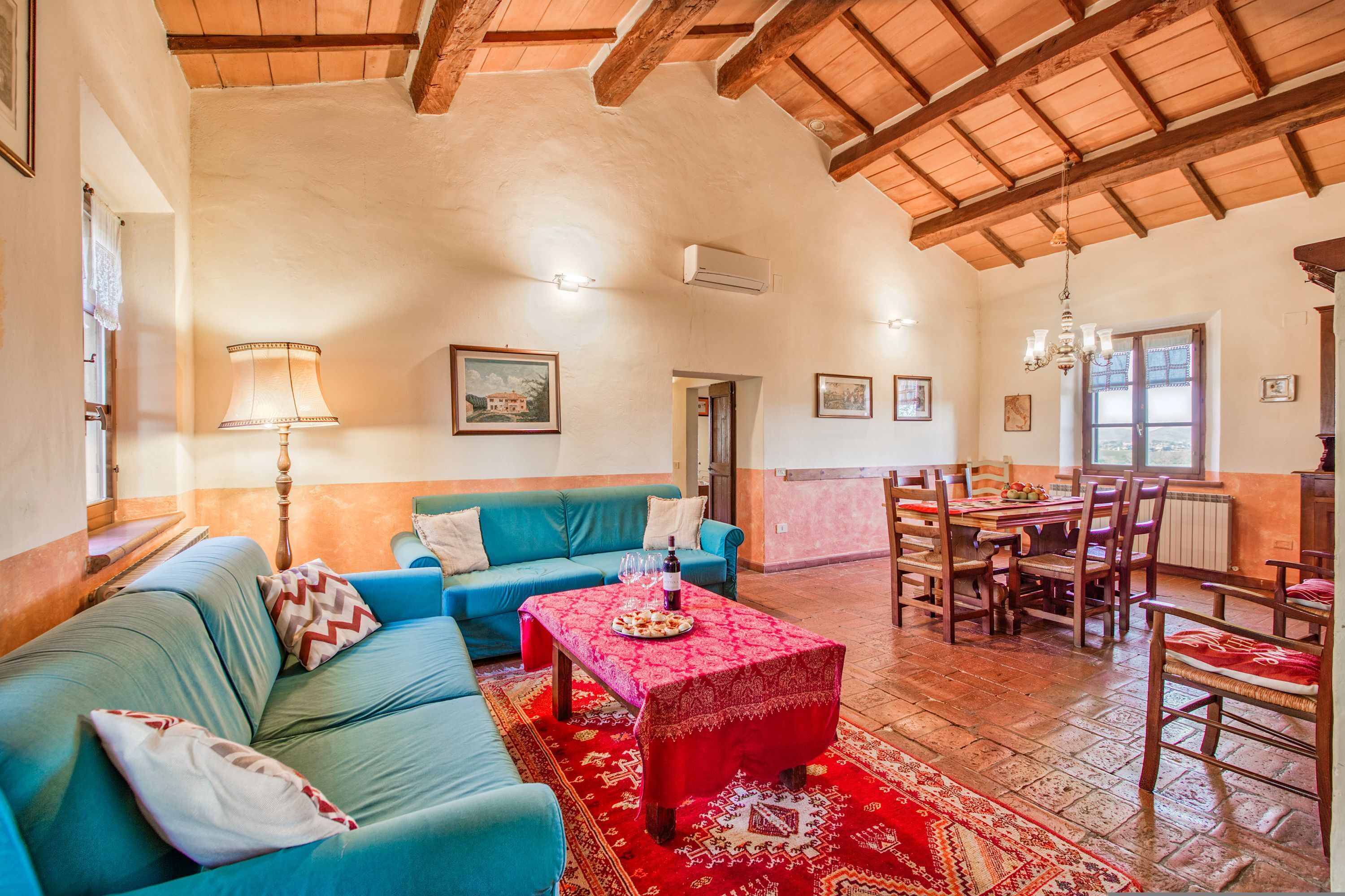 A cozy living room with a blue sofa, a red table, and a wooden ceiling.