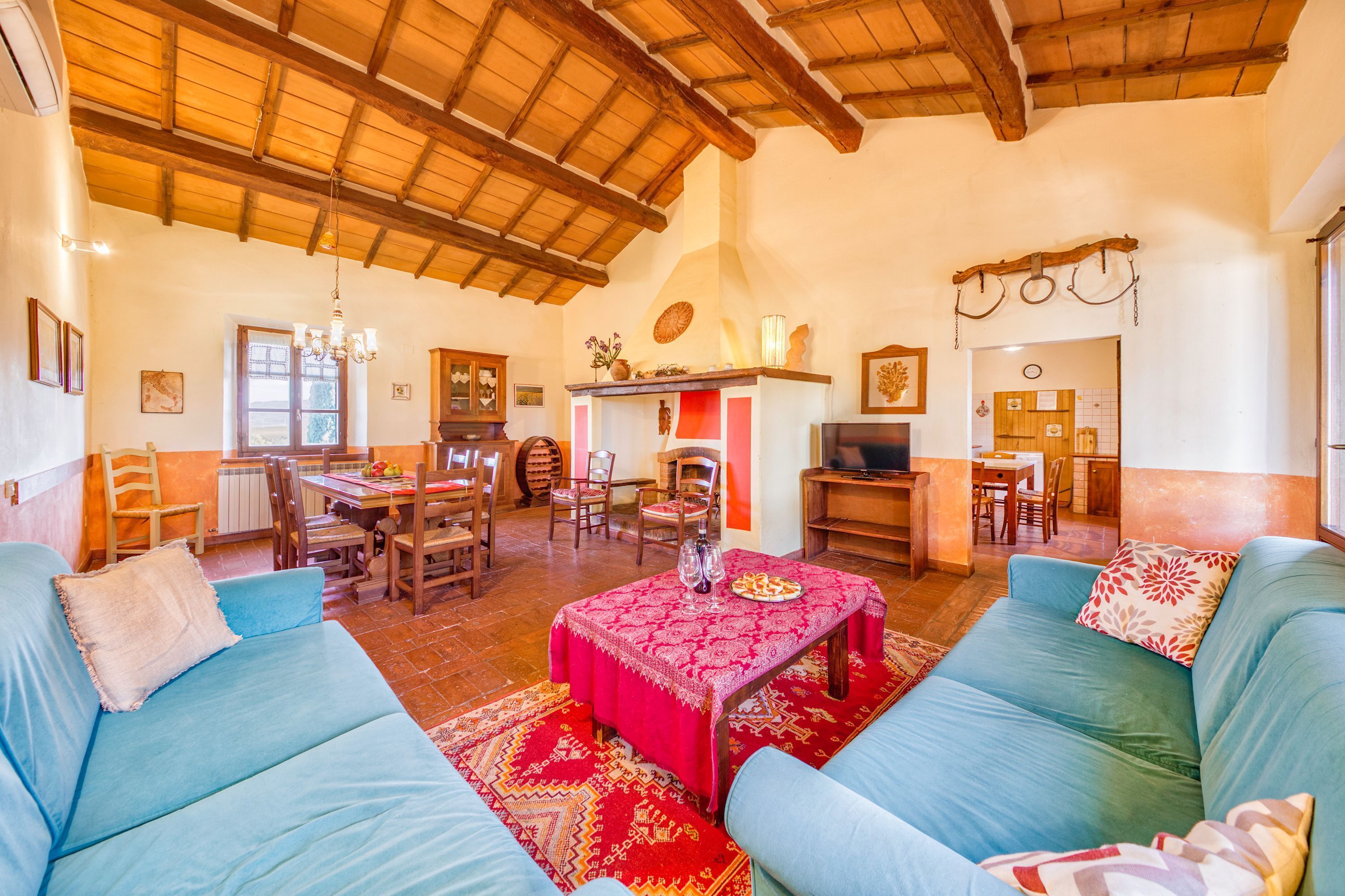A spacious living room with a high wooden ceiling, a dining area with wooden furniture, and a kitchen area.