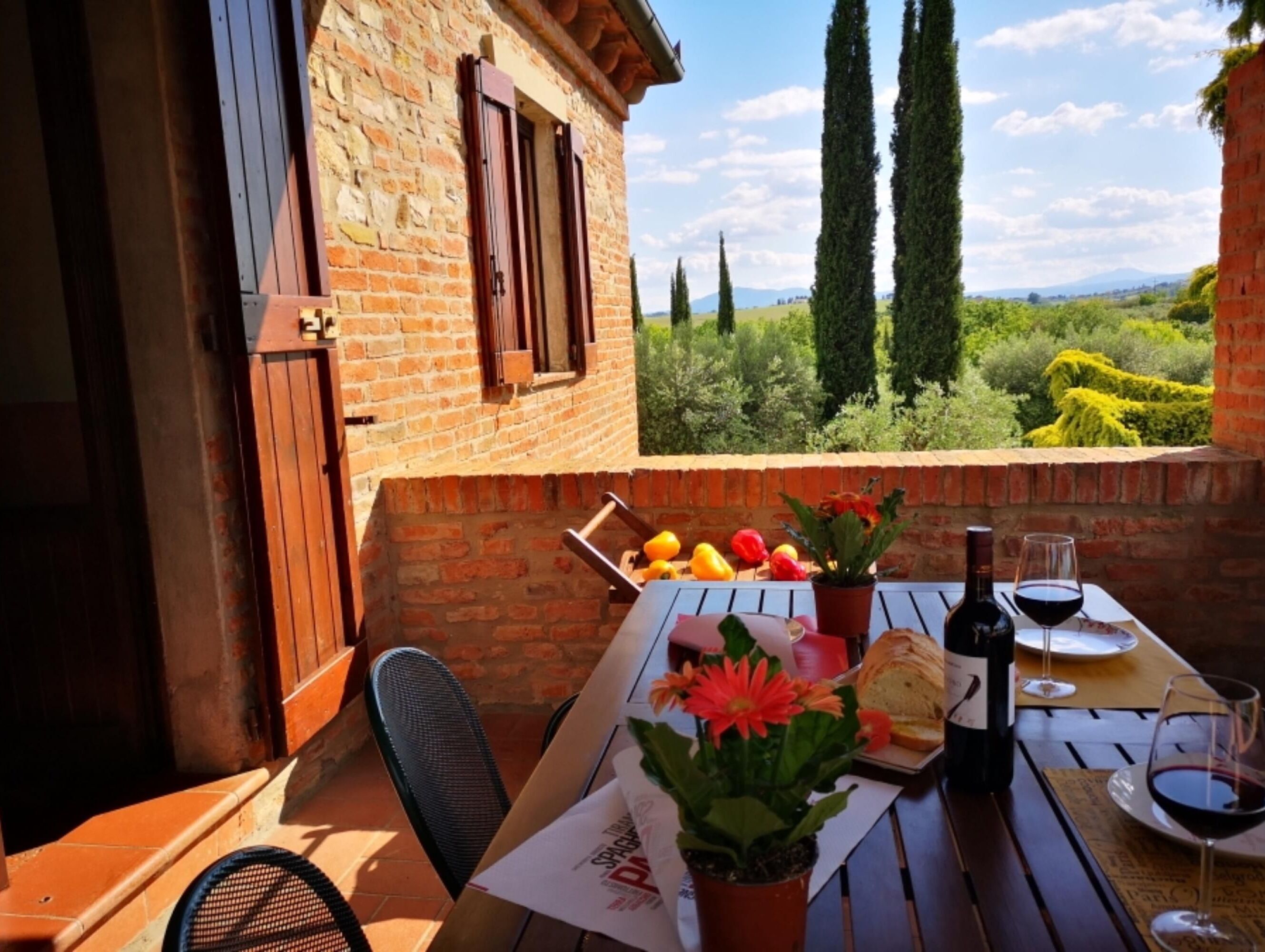 A patio with a table set for dining, a bottle of wine, and a glass of red wine.