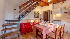 A dining area with a wooden staircase, a red sofa, a dining table set for two, and a kitchen area with cabinets and a countertop. - Rosehip apt With Shared Pool (Castiglione del Lago)