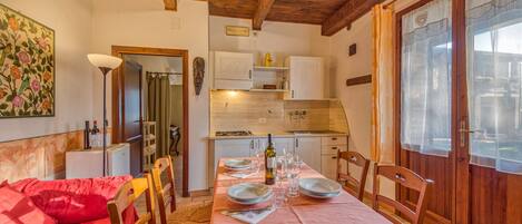 A cozy dining area with a table set for two, wooden chairs, a red sofa, and a kitchen in the background.