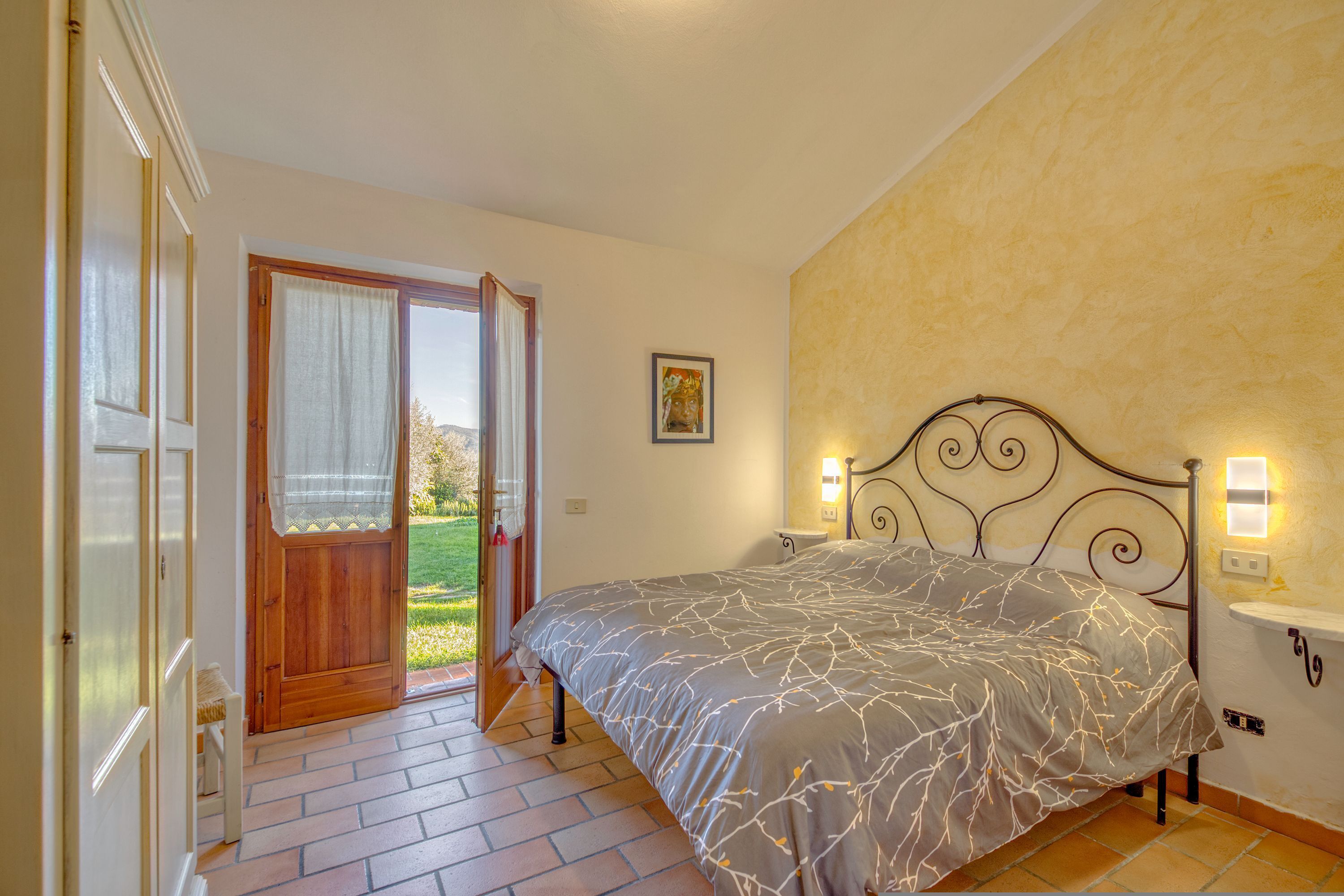 A bedroom with a bed, a door leading to a balcony, and a wall-mounted light fixture.