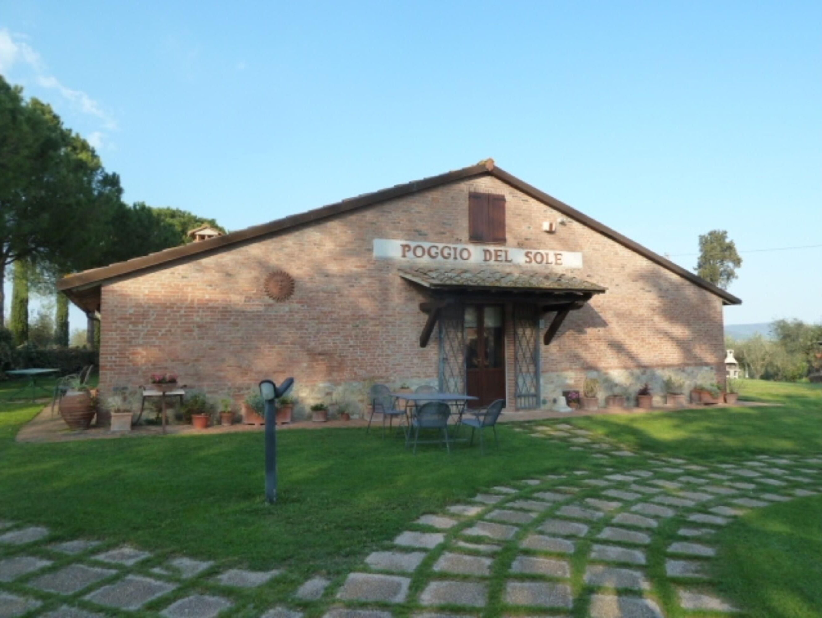 Un rústico edificio de ladrillo llamado POGGIO DEL SOLE con un pequeño patio y asientos al aire libre.