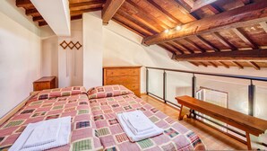 Ein Schlafzimmer mit Holzboden, einem Bett mit kariertem Überwurf, einem Nachttisch und einer Bank am Fenster.