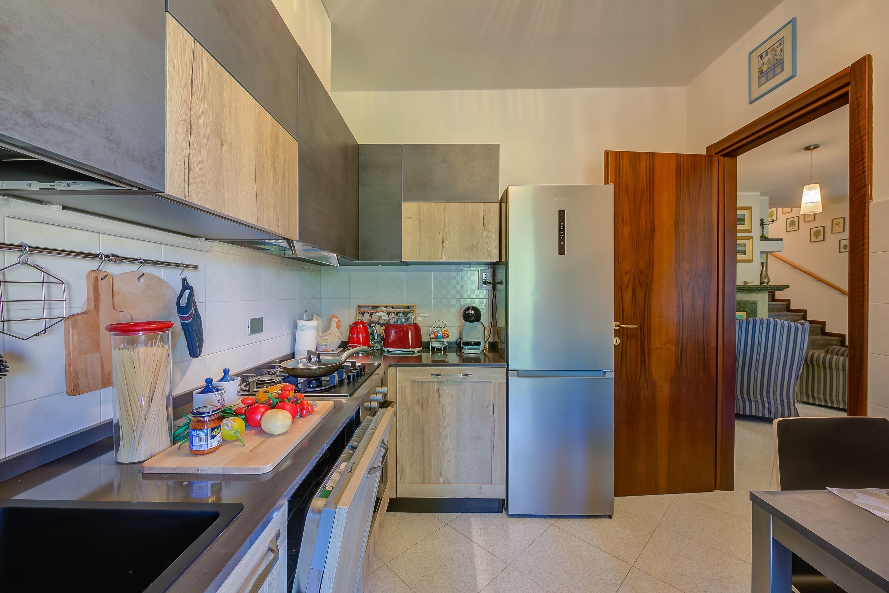 A modern kitchen with wooden cabinets, a stainless steel refrigerator, and a wooden countertop with various kitchen items.