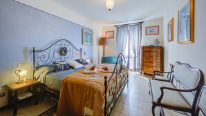 Een slaapkamer met een bed, nachtkastje, lamp, kaptafel, stoel en gordijnen.