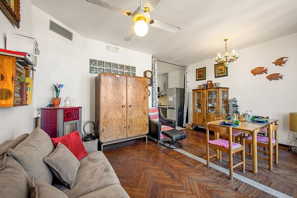 Un salon comprenant un canapé, un meuble en bois, une table à manger avec des chaises et un ventilateur de plafond.