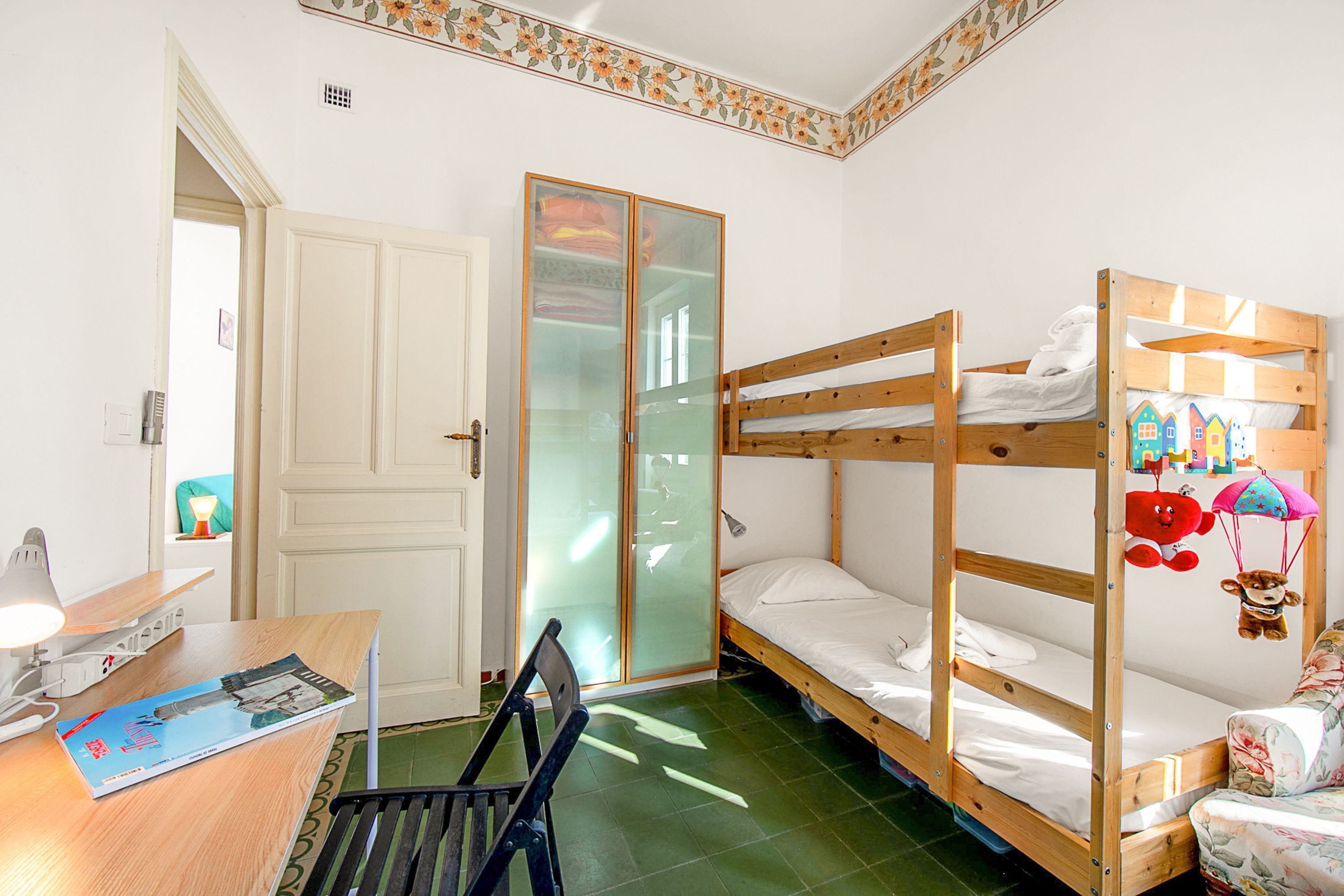 Ein Schlafsaalzimmer mit Etagenbetten, einem Schreibtisch mit Lampe, einem Stuhl und einem Kleiderschrank.