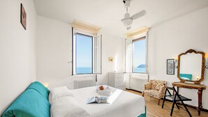 A bedroom with a bed, a chair, a table, and a view of the sea. - La Vie Enchanting Sea View (Alassio)