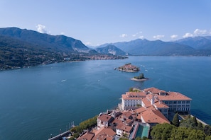 A coastal town with a prominent building complex featuring multiple buildings with red-tiled roofs, situated by a large body of water with boats and a small island in the distance.