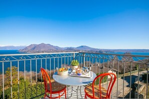 A balcony with a table set for two, overlooking a scenic view of mountains and a body of water. - Penthouse The Magnifique View (Stresa)